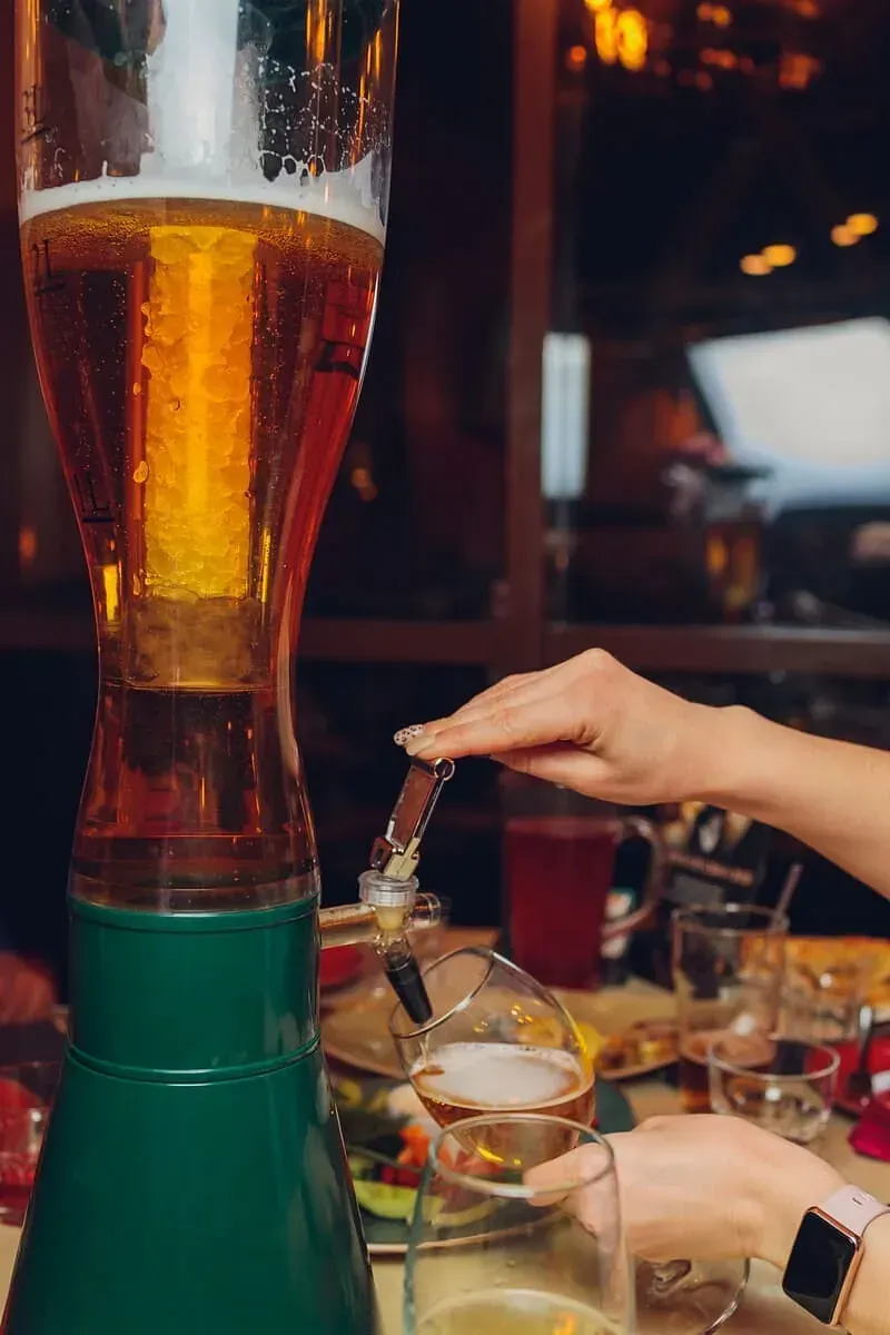 Una mujer está sirviendo cerveza en un vaso desde un dispensador de cerveza alto.