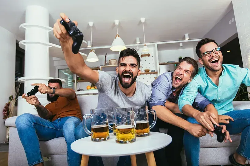 Un grupo de hombres está sentado en un sofá jugando videojuegos y bebiendo cerveza.