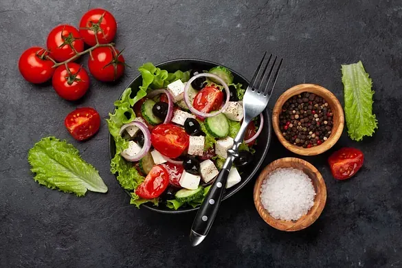 Una ensalada en un bol con un tenedor y tomates en una mesa.