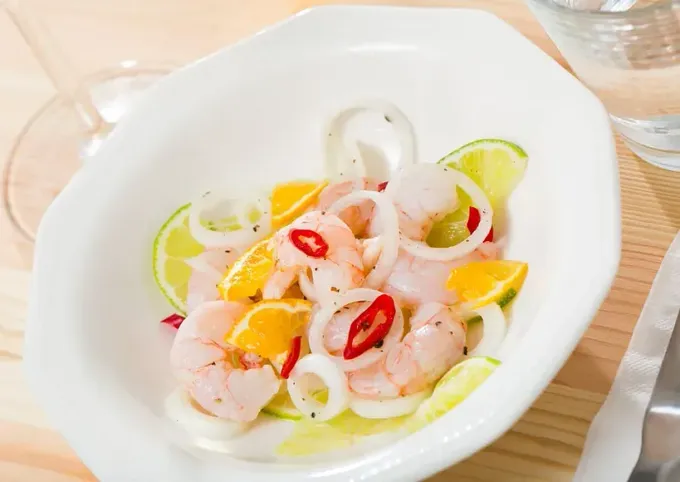 Un tazón blanco lleno de camarones, calamares, cebollas y limas.