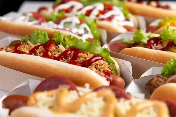 Un montón de perritos calientes con ketchup, mostaza y lechuga encima.