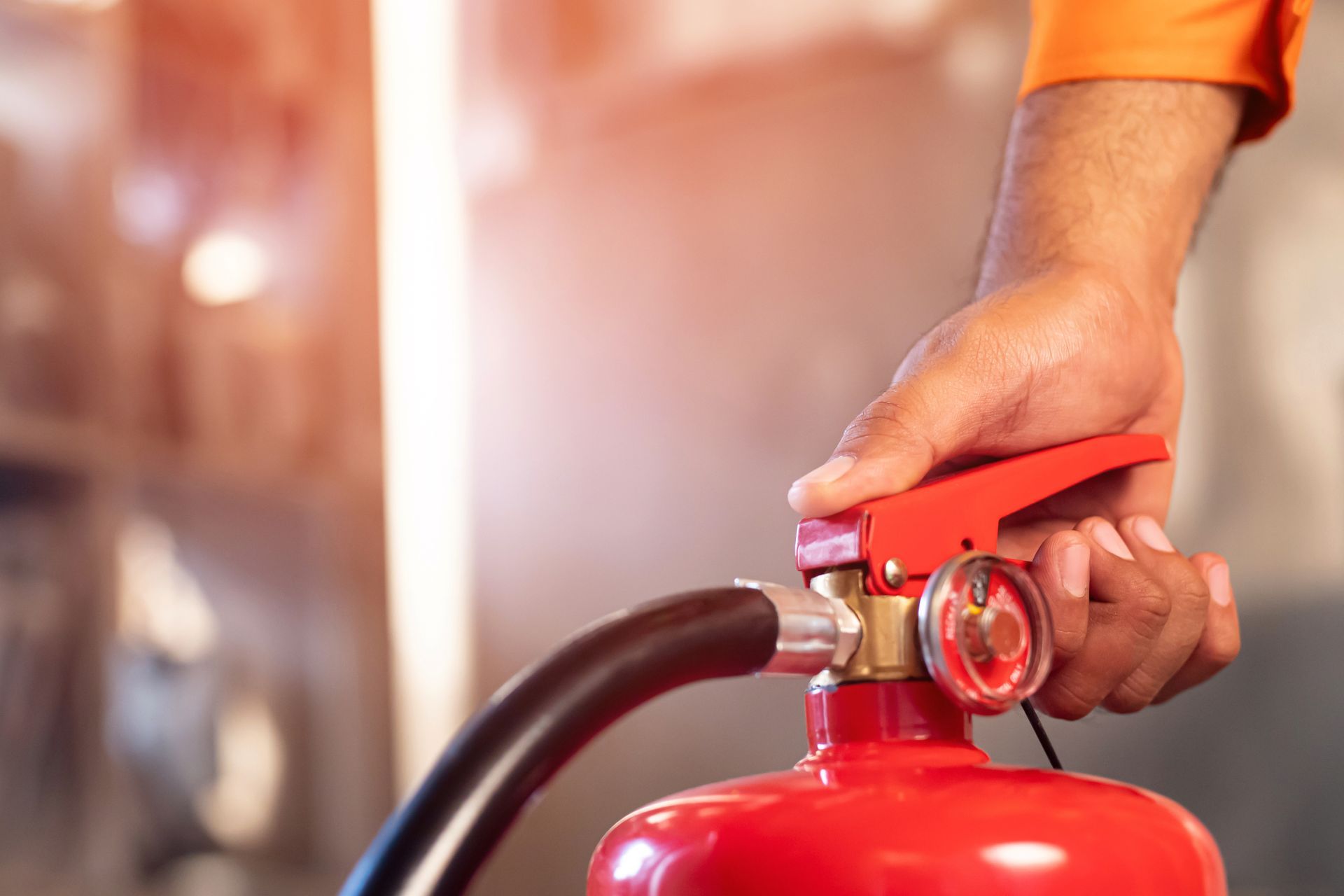 Main d'une personne tenant un extincteur rouge, prête à l'utiliser. Lumière vive en arrière-plan.