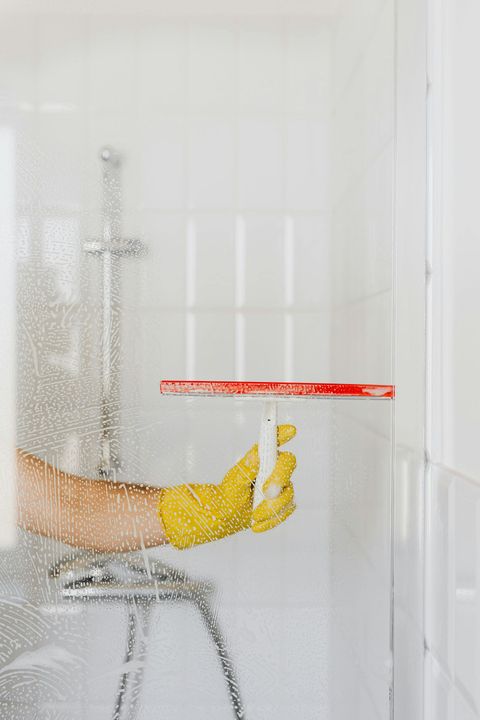 Una persona está limpiando la puerta de una ducha con una escobilla de goma.