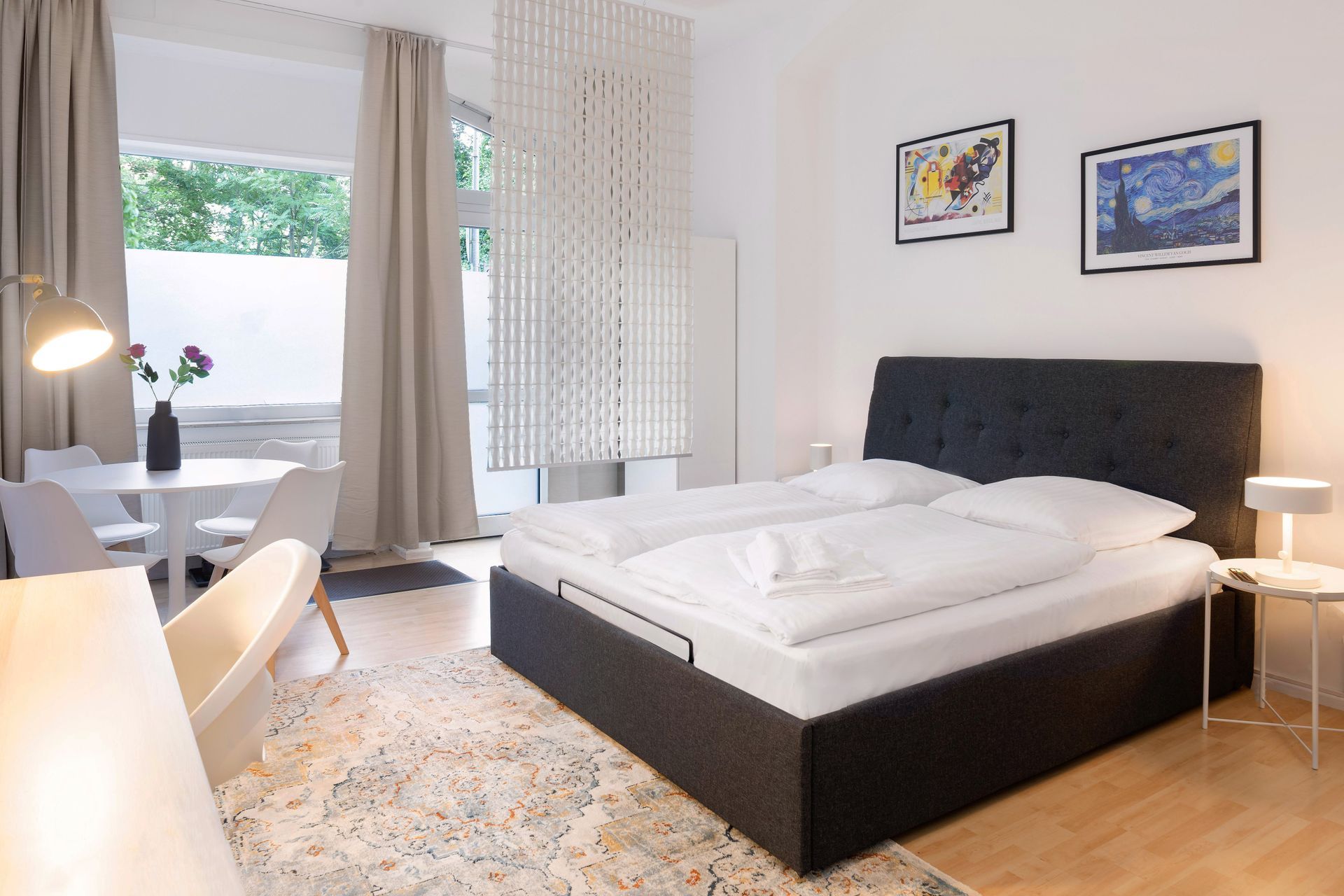 Bedroom with a bed, table, and artwork. A bright space with a decorative room divider.