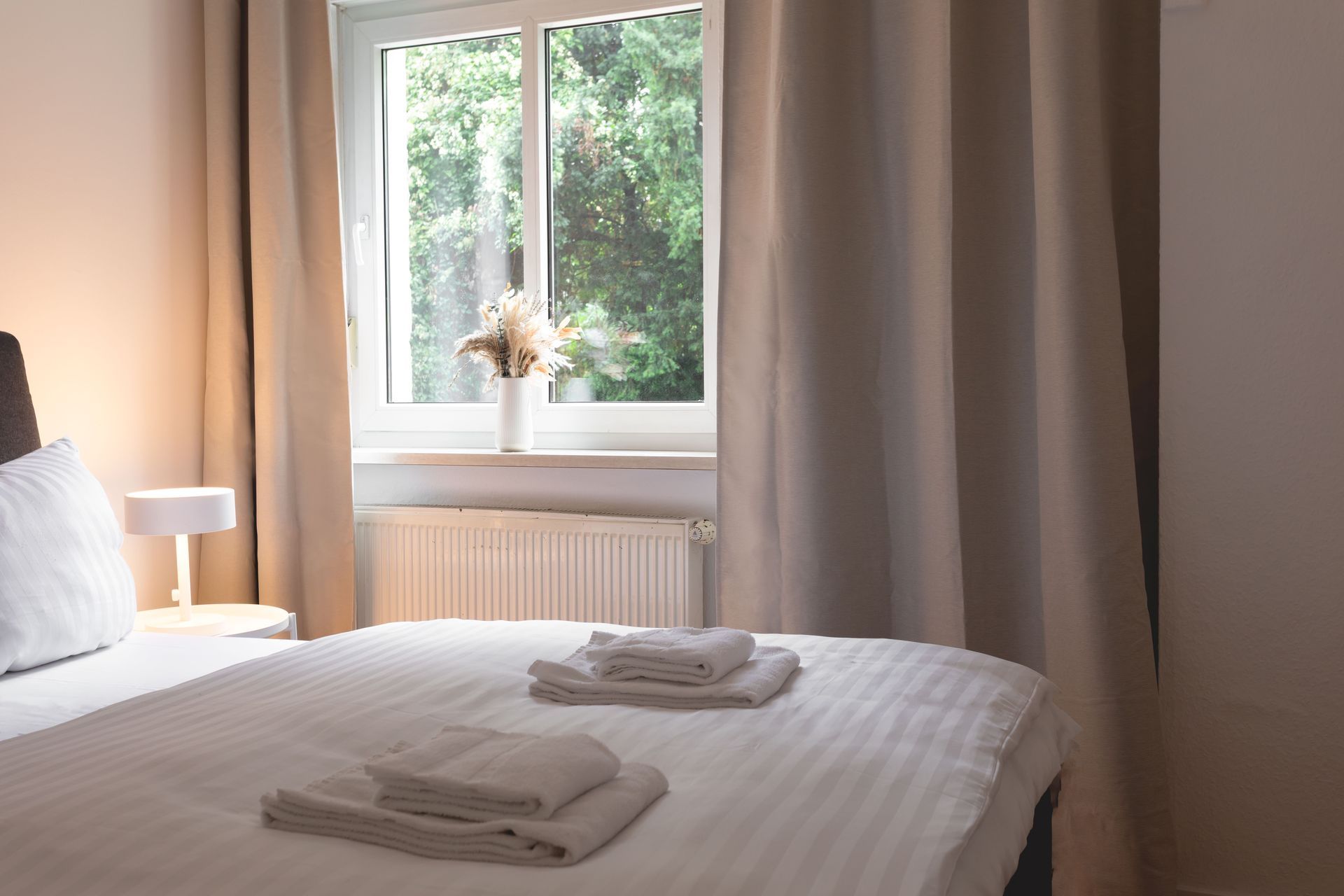 Bedroom with a bed, window, curtains, a lamp, and towels.
