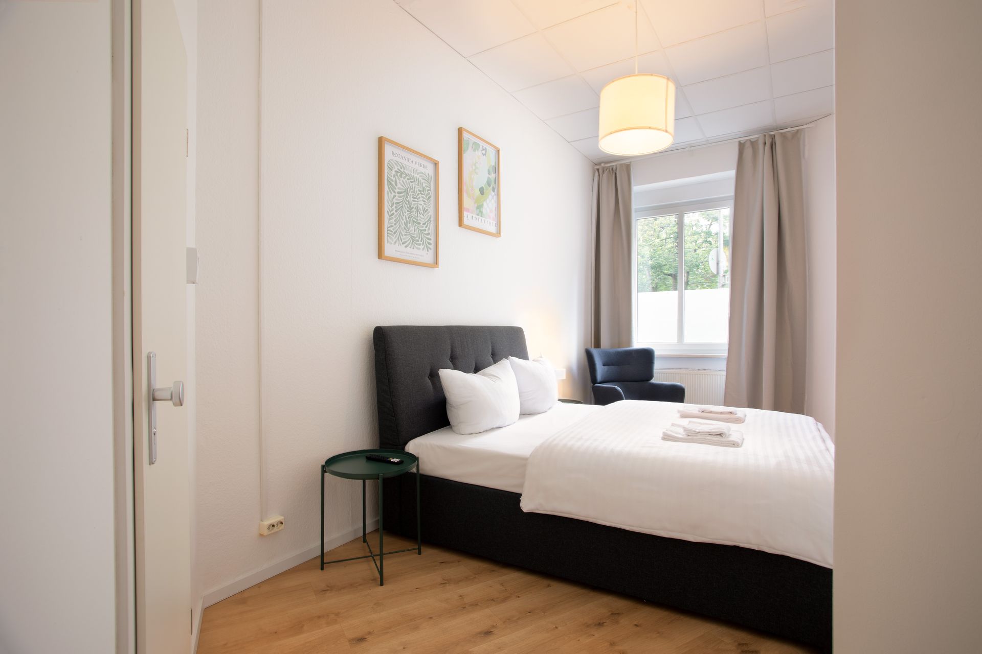 Bedroom with bed, side table, window, and artwork.