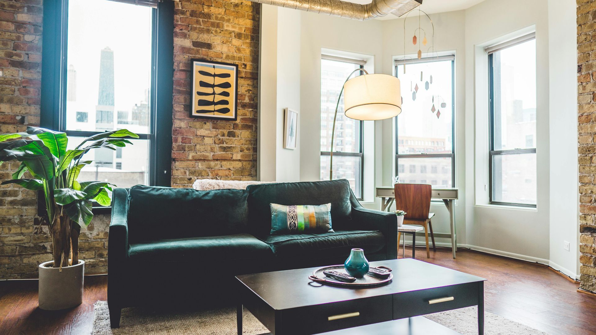 Living room with green sofa, brick wall, large windows, and dark coffee table.