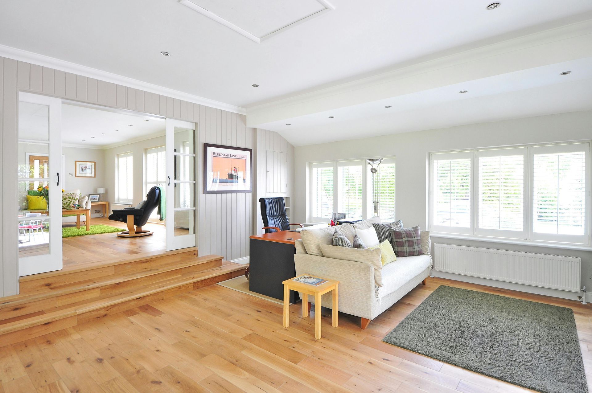 Spacious living room with hardwood floors, a white sofa, and a view into another room through glass doors.