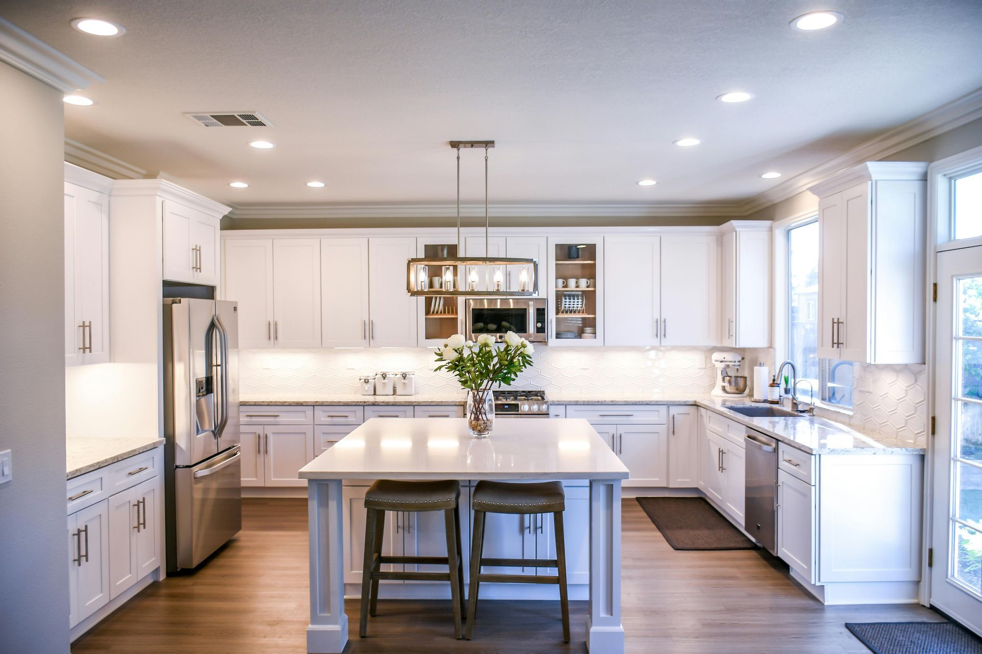 Bright white kitchen with island and stainless steel appliances. Wooden floors, white cabinets, and a floral centerpiece.