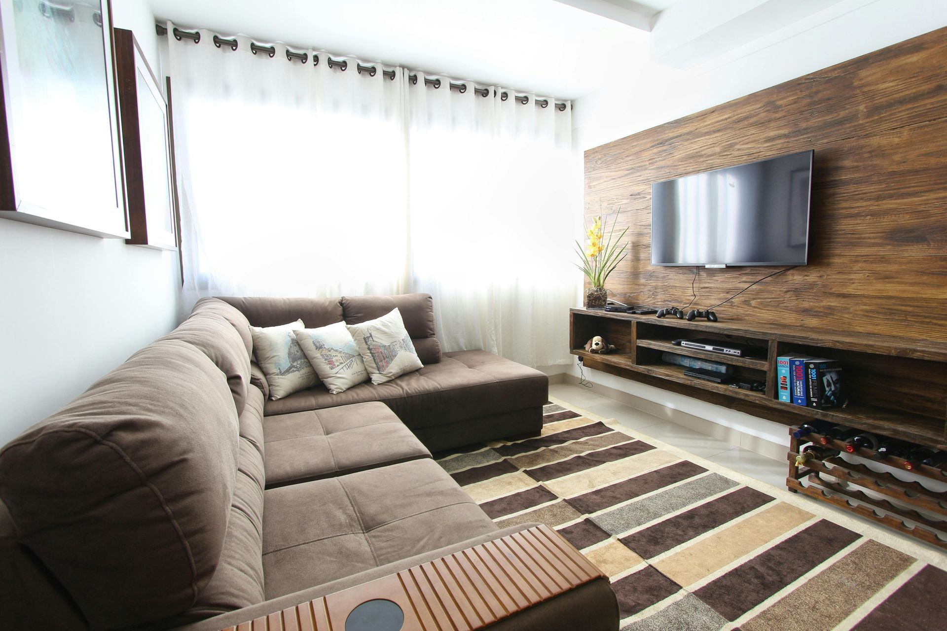 Cozy living room with brown sectional sofa, TV on wooden wall, and patterned rug.