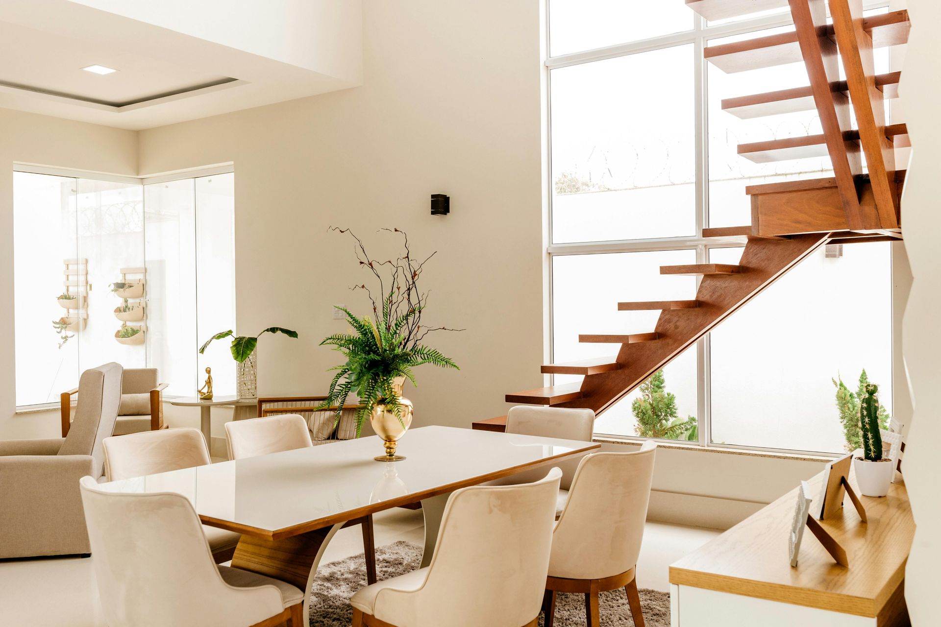 Dining room with white table, chairs, stairs, and tall windows.
