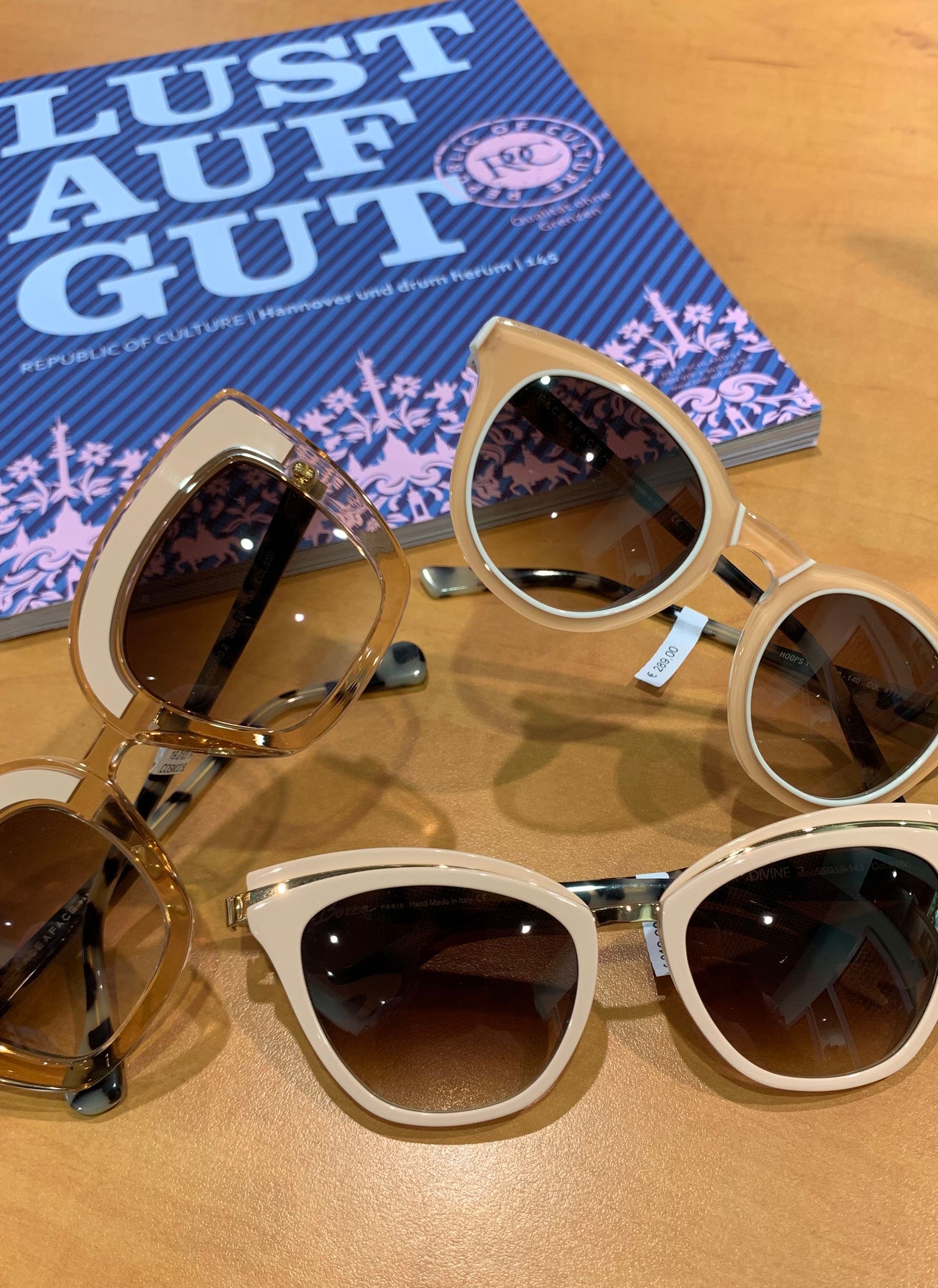 Drei Sonnenbrillen liegen auf einem Tisch neben einem Buch mit dem Titel „Lust auf Gut“