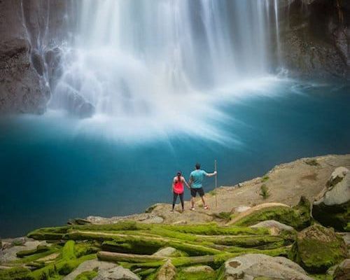A man and a woman are standing on the edge of Catarata del Toro waterfall