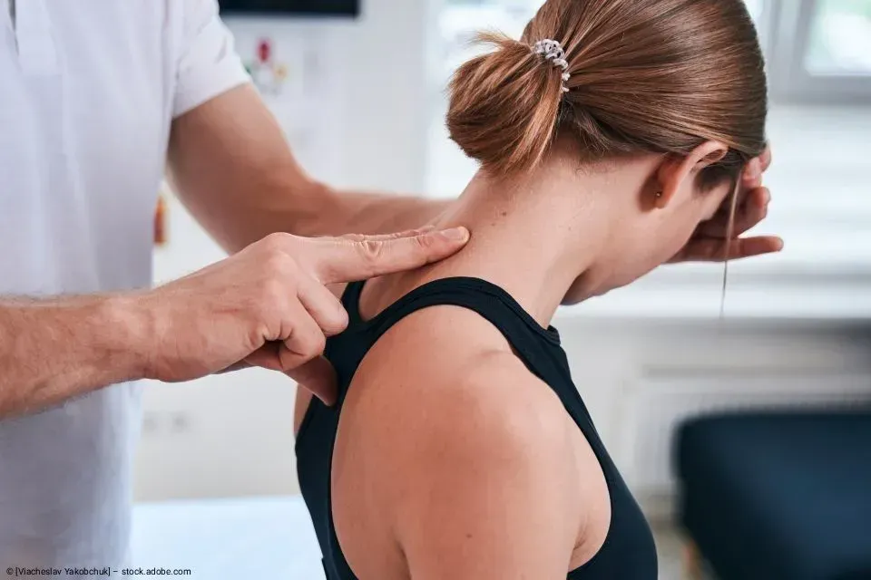 Physiotherapeut drückt während einer Nacken- und Schulteruntersuchung auf den oberen Rücken einer Frau.