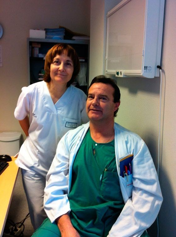 Un hombre con bata de laboratorio se sienta junto a una mujer con uniforme médico.