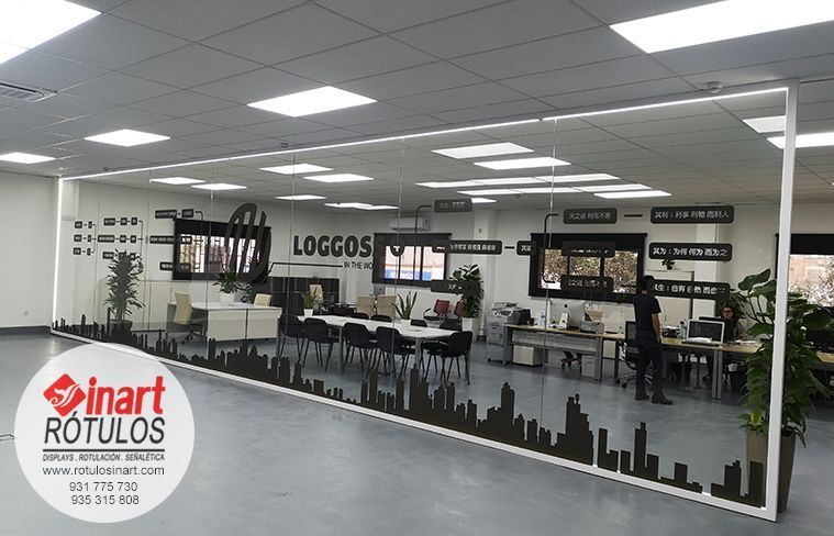 Oficina diáfana con escritorios, una mesa de conferencias y un gran ventanal con un vinilo negro que muestra el perfil urbano de la ciudad a la altura de los ojos.