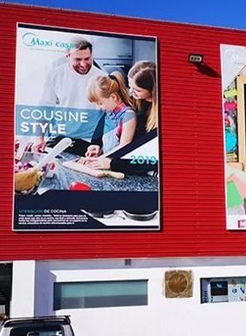 Un gran anuncio exterior en un edificio rojo que muestra a una familia preparando comida en una cocina, titulado