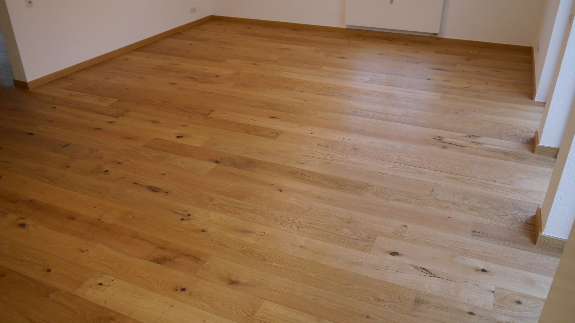 Ein leerer Raum mit Holzboden und weißen Wänden.