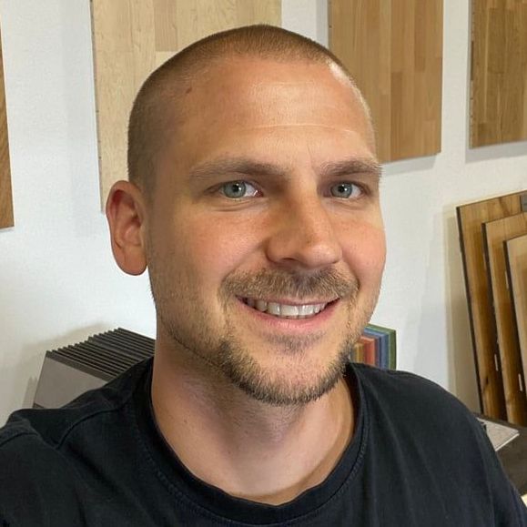 Ein Mann mit Bart und schwarzem Hemd lächelt in die Kamera.