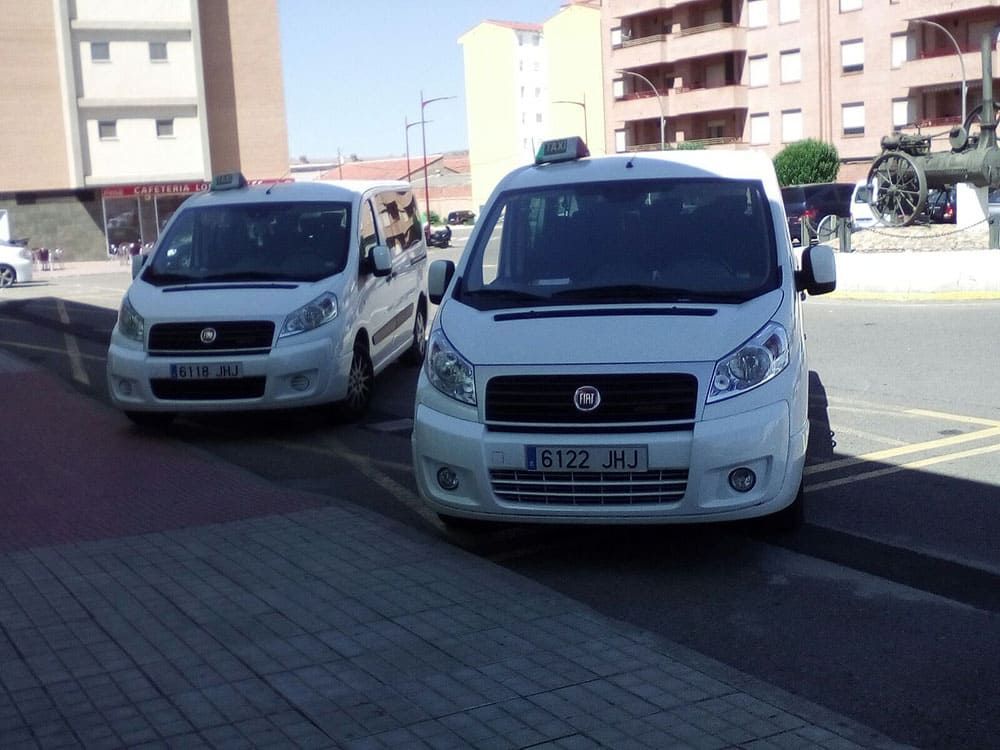Dos furgonetas Fiat blancas aparcadas en una calle cerca de un edificio y una escultura.