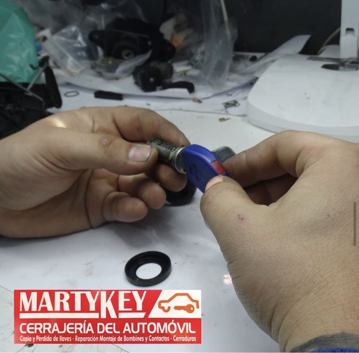 Manos manipulando una llave de coche, sosteniéndola con un llavero. Hay una junta negra sobre la mesa.