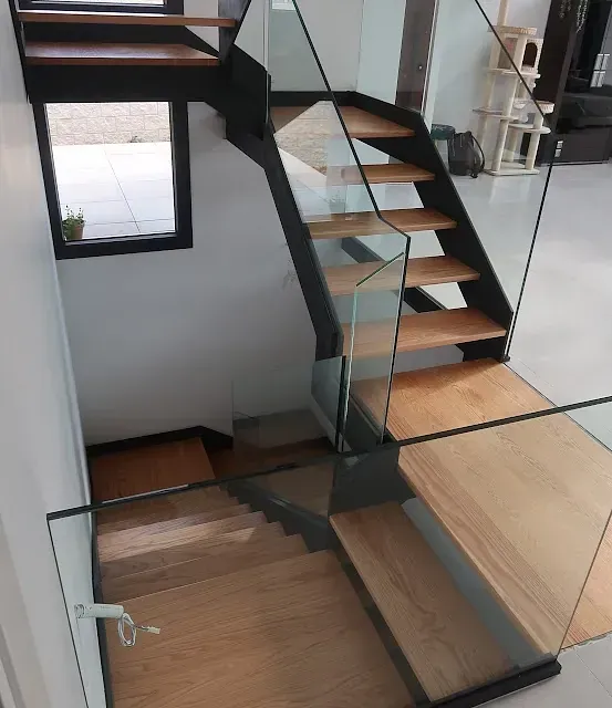 Escalera de madera y cristal en una casa moderna. Estructura de metal negro, peldaños de madera clara y barandilla de cristal.