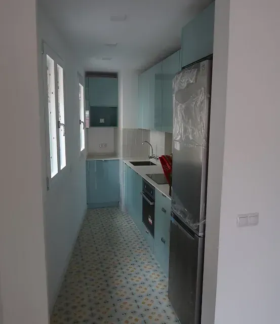 Cocina estrecha con gabinetes de color azul claro, refrigerador de acero inoxidable y piso de baldosas estampadas.