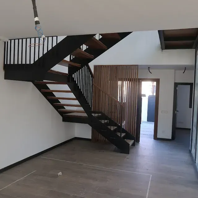 Interior moderno con escalera de madera y negra, paredes blancas y biombo de listones de madera.