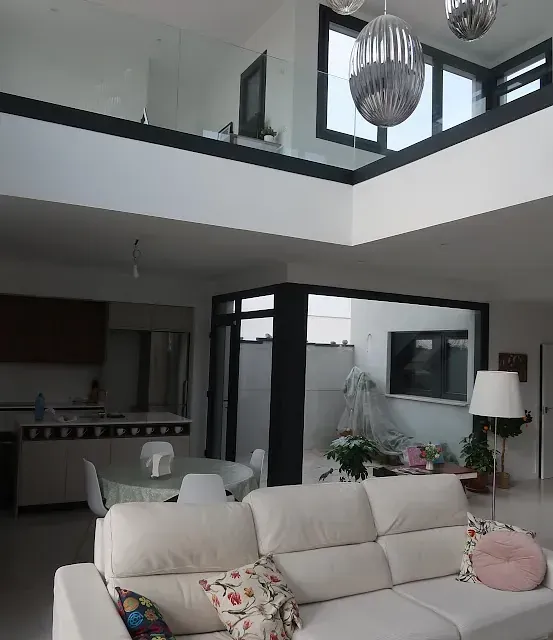 Moderna sala de estar blanca con loft y cocina abierta, con sofá blanco y grandes ventanales.