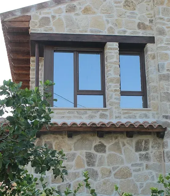 Ventanas con marcos marrón oscuro en la pared de piedra. Toldo de madera marrón en la parte superior.