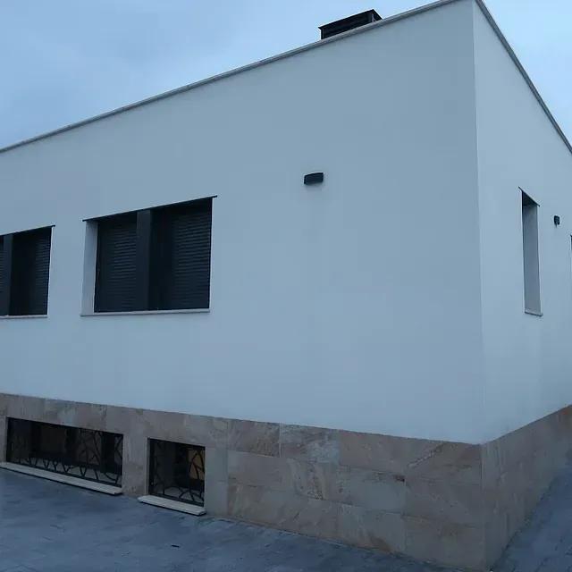 Edificio moderno blanco con base de piedra color canela y ventanas con marco negro.