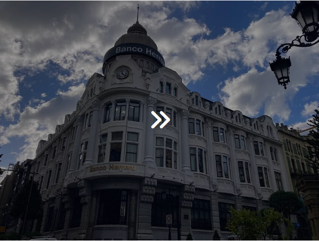 Edificio histórico del Banco Bilbao Vizcaya Argentaria con cúpula y reloj, frente a un cielo azul.
