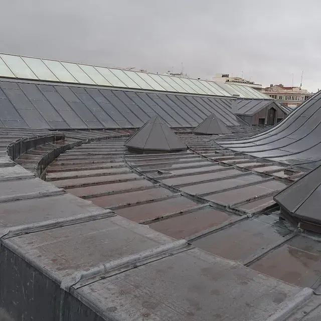 Techo de metal con lucernarios y respiraderos triangulares bajo un cielo nublado.