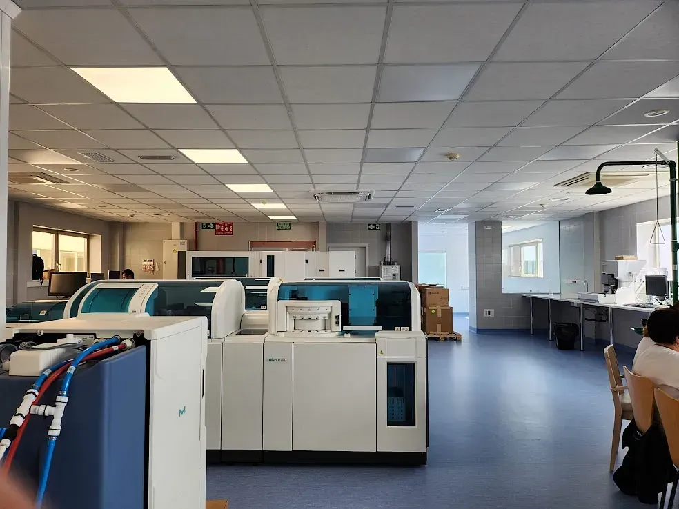 Laboratorio con máquinas médicas, piso azul, paredes blancas, iluminación cenital.