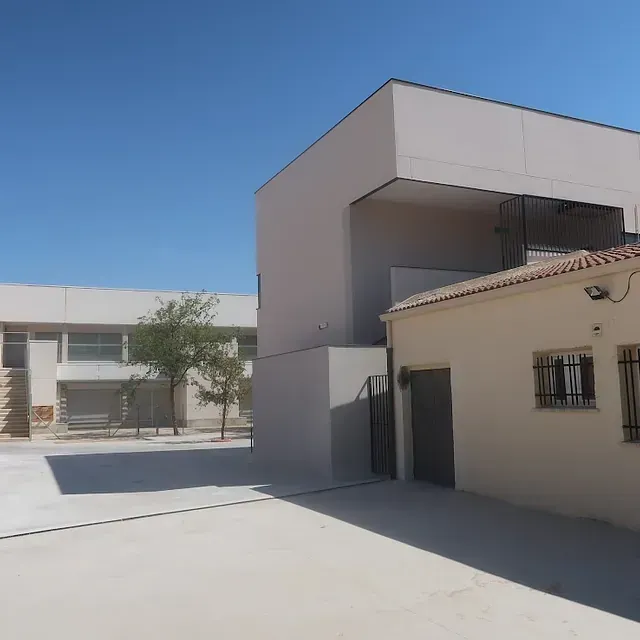 Vista exterior de dos edificios, uno blanco y otro beige, en un día soleado.