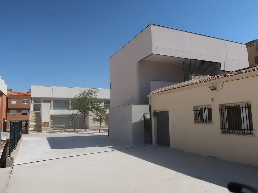 Vista exterior de edificios en un día soleado; paredes de colores claros, suelo de hormigón, cielo azul.