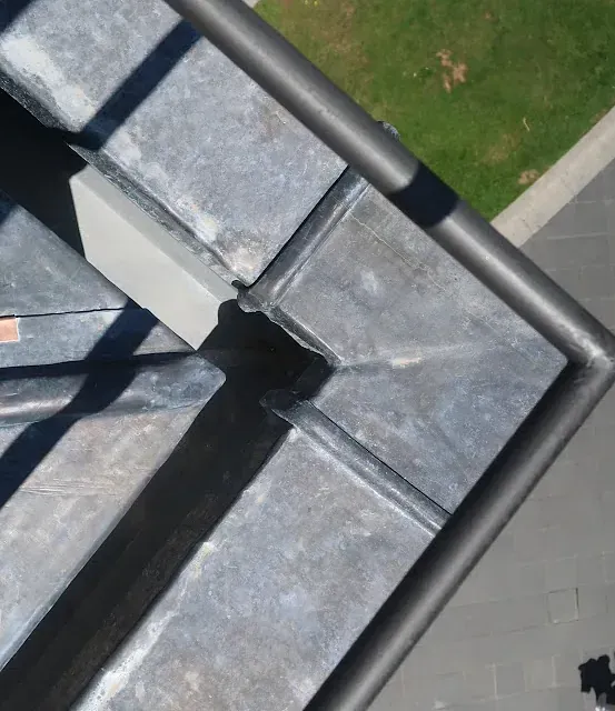 Esquina de techo de plomo con tapajuntas metálico gris oscuro y una sección de canalón negro.