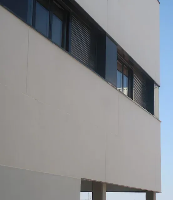 Edificio blanco moderno con ventanas horizontales y contraventanas oscuras contra un cielo azul.