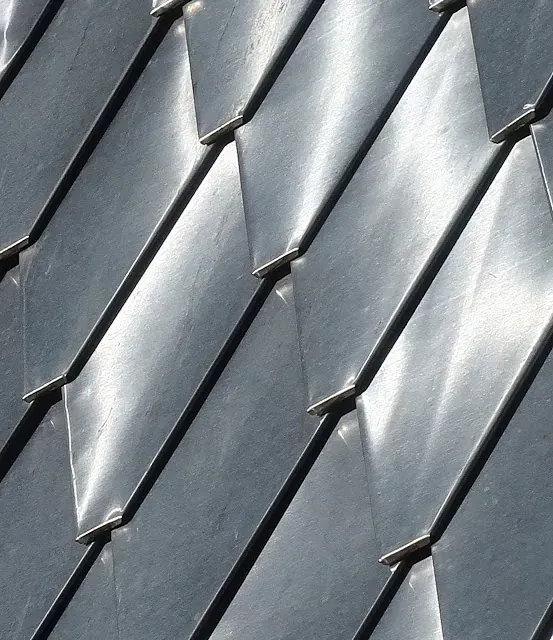 Primer plano de baldosas metálicas grises en diagonal, que reflejan la luz y forman una superficie texturizada.