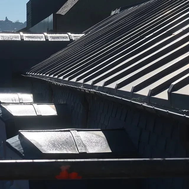 Primer plano de un techo de metal oscuro con paneles superpuestos, que muestra un borde curvo y sombras.