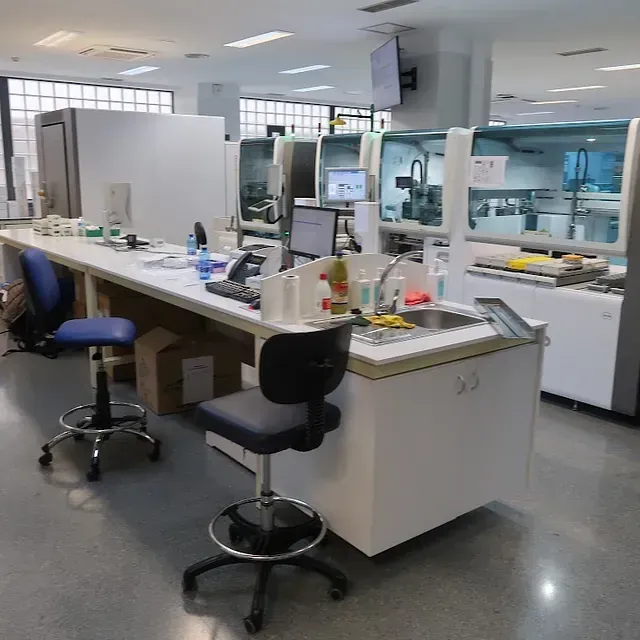 Laboratorio con mostradores blancos, taburetes, máquinas y equipos.