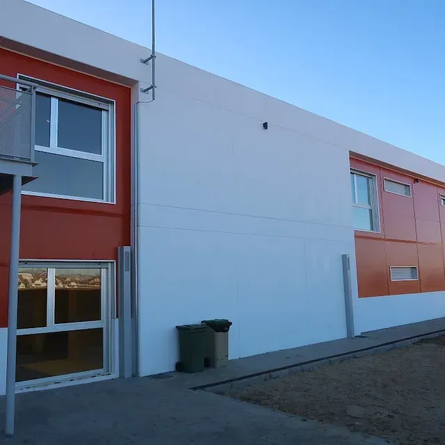 Exterior de un edificio moderno con paneles, ventanas y botes de basura de color naranja y blanco.