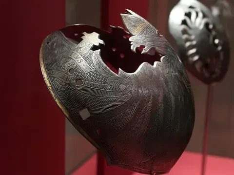 Protector de brazo de metal plateado adornado, con recortes en forma de pájaros y patrones grabados en exhibición.