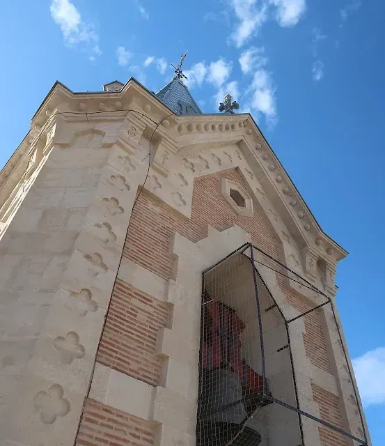 Exterior de capilla de piedra con detalles de ladrillo rojo, contra un cielo azul.