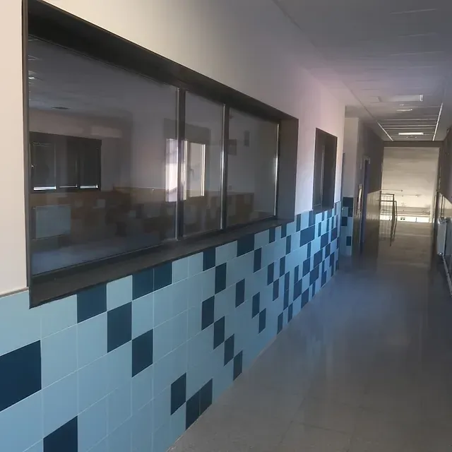 Pasillo con grandes ventanales, pared de azulejos azules y blancos y una perspectiva larga y estrecha.