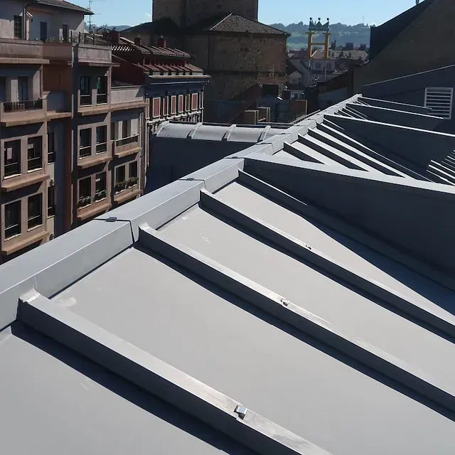 Techo de metal gris con fondo de ciudad, cumbreras en ángulo y edificios.