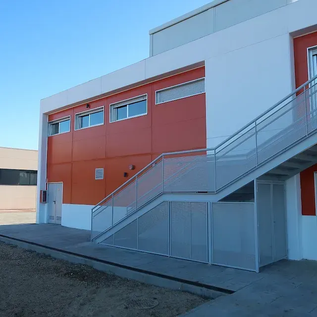 Exterior de un edificio moderno con paredes naranjas y blancas, escalera de metal y cielo azul.