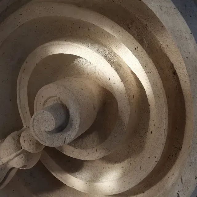 Primer plano de un detalle arquitectónico de piedra en espiral de color claro con sombras y texturas fuertes.