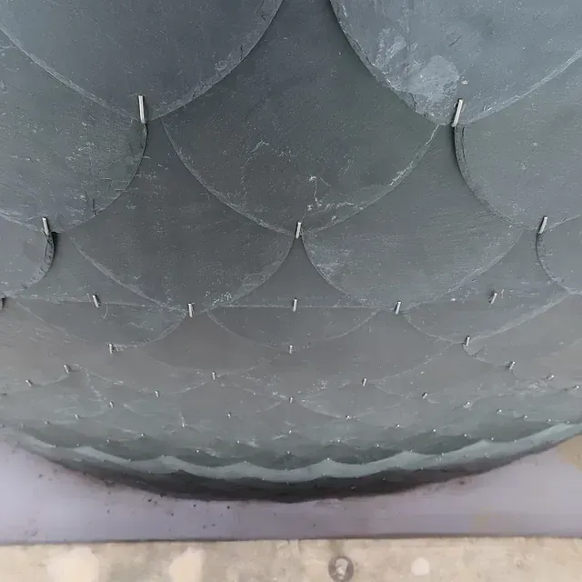 Vista aérea de un techo de color oscuro, en forma de escamas, sobre una superficie curva.