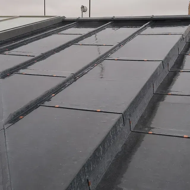 Primer plano de un techo de metal oscuro y húmedo con costuras y sujetadores visibles.